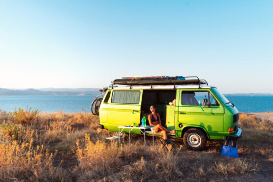 Young attractive female sitting in old timer camper van on a hill above the beach looking at the golden light of sunset. Young attractive female sitting in old timer camper van on a hill above the beach looking at the golden light of sunset.